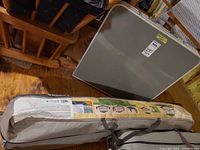 Beige Woods screen shelter in carry bag alongside folded metal table