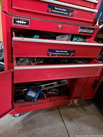 Overall view of open bottom section of red cabinet showing multiple hand tools including level and saw