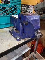 Side view of blue bench vise showing jaws, handle, and swivel base