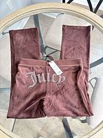 Front view of mauve velour sweatpants with rhinestone Juicy logo and hang tag