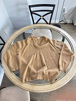 Full view of camel tan V-neck sweater laid flat on glass table