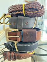 Stacked view of multiple leather belts showing colors, buckles, braided strap
