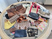 Group shot showing all handbags, totes, clutches, wallets and pouches laid out on glass table