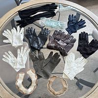Overview of assorted gloves and three beaded collars on glass table