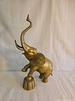 Side view of brass elephant statue showing pedestal and raised trunk