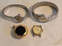 Four watches laid out: two silver-tone expansion-band wristwatches, gold-tone watch head, gold-tone & black digital pendant