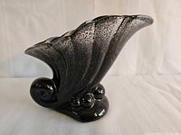 Right-side view of black speckled cornucopia vase showing scroll base and bead feet