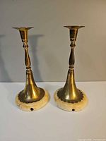 Front view of two matching brass candlesticks on marble bases