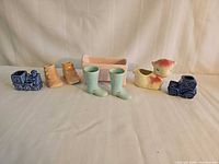 All eight ceramic pieces lined up: blue train, peach shoes, Haeger cradle, aqua boots, lamb, blue car