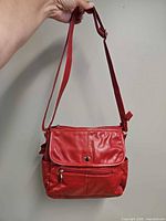 Front view of red leather shoulder bag hanging by adjustable strap, showing flap and exterior zip pocket