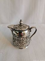 Front view of ornate silver-plated syrup jug