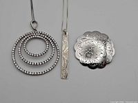 Front view: round cubic zirconia pendant on chain, rectangular engraved pendant, scalloped floral brooch
