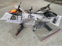 Two RC helicopters, manuals underneath, spare parts in bags