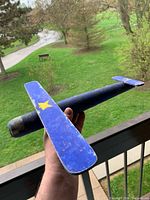 Blue painted hardwood airplane held in hand showing fuselage, wing, tail
