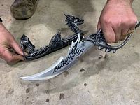 Hand holding curved dragon dagger with display stand visible