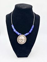 Front view of necklace on stand showing silver face pendant and blue trade beads