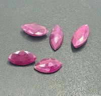 Five faceted marquise-cut ruby gemstones displayed on grey surface