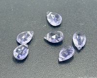 Six pear-cut light violet tanzanite gemstones on dark background