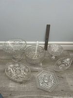 Group of six pressed glass dishes and one serving spoon displayed for scale