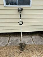 Full view of gas string trimmer leaning against wall showing entire length, shaft, handle and cutting head