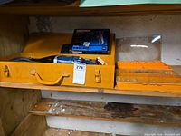 Shelf with yellow metal toolbox opened showing AEG saw, Craftsman drill box and orange hardware case