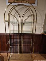 Full view of brass-tone arched étagère with glass shelves
