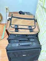 Stack showing tan messenger bag on top of brown hard briefcase and black soft briefcases