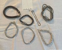 All seven silver-tone costume bracelets laid out on cloth