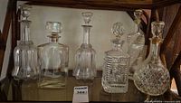Group shot of six clear glass and crystal decanters with stoppers on shelf