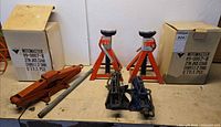 Pair of boxed Motomaster axle stands, black scissor jack, orange lever jack and crank handle on workbench