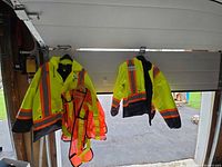 Two jackets and one vest hanging on garage door for overall view