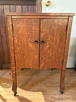 Front view of wood cabinet showing two doors, knobs, lock, legs and castors