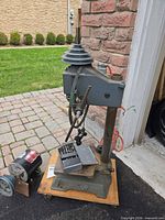 Rockwell drill press body on wooden board with stepped pulleys, quill feed, hanging chuck key and drill bit index set; detached motor visible