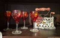 Four ruby red etched wine glasses and one ceramic decorative iron on shelf