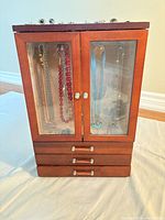 front view of wooden jewelry armoire showing doors, drawers and items inside