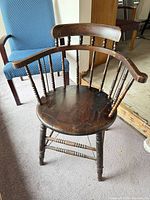 Front view of wooden spindle-back Windsor chair showing seat, arms, legs, and overall wear