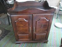 Front view showing two paneled doors, brass pulls, wood finish