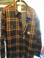 Front view of black/tan plaid Carhartt flannel sherpa lined shirt jacket on hanger