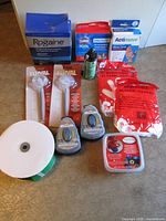 All items in lot arranged together: Rogaine box, Clorox test kit, Actimove brace box, Dri-Slide bottle, two Fluval shrimp nets, two Kiwi shoe polish sponges, plastic gloves pack, ribbon roll, wax melts
