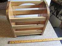Front angled view of wooden slatted magazine rack with ruler for scale