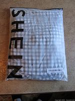 Factory-sealed Shein polybag containing gingham dress