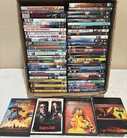 Front view showing approximately 60 DVD cases stacked in a box with four cases laid out in front