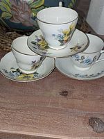 Front view of three stacked teacup and saucer sets showing floral patterns and gold trim