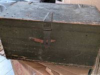 Front view showing olive drab trunk, hasp closure, metal reinforcements, paint wear