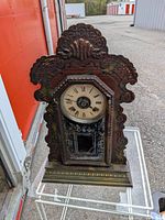 Front view of carved wooden mantel clock showing dial and reverse-painted glass