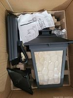 Lantern components in box including fixture body, wall plate, scroll arm, hardware and paperwork