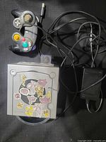 Top view of silver GameCube with stickers, wired controller, power adapter visible