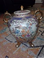 Front view of tripod pottery vase with lid, showing bird and floral motif, gold handles and feet