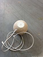 Top view of spherical white Apple HomePod mini with attached white USB-C cable coiled beside it