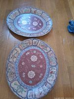 Two oval decorative ceramic plates on wooden floor